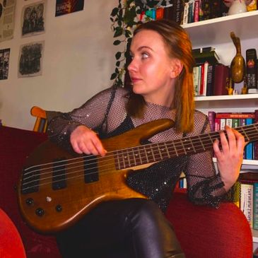 A young woman playing a bass guitar on a red couch in a cozy room.