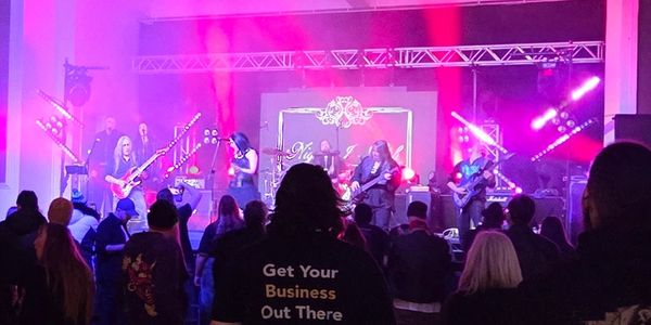 Live band performing on stage with audience watching under colorful lights.