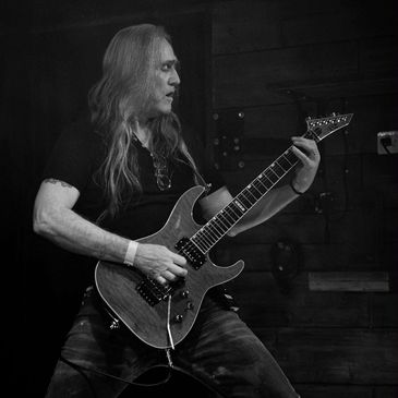 Long-haired musician passionately playing electric guitar on stage.