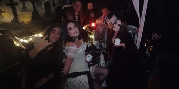 Group in gothic costumes poses in a dark, eerie graveyard setting.