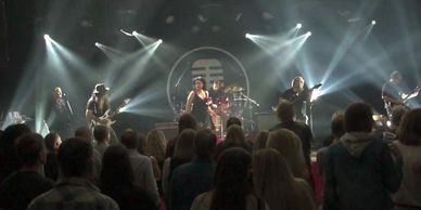 A rock band performing on stage with bright lights and an audience.