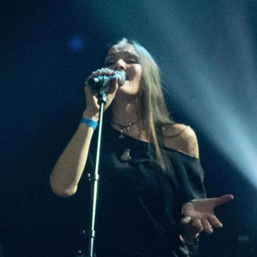 A female singer passionately performing on stage with dramatic lighting.