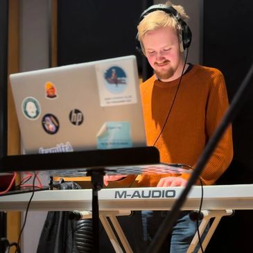 Man playing keyboard in a recording studio with headphones on.