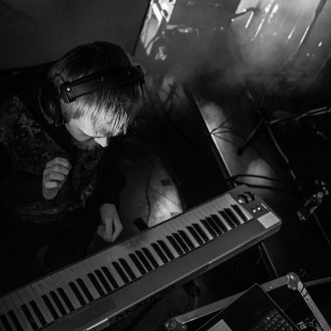 Person wearing headphones playing a keyboard in a dimly lit room.