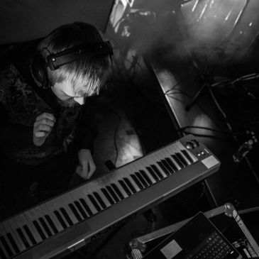 Person wearing headphones playing a keyboard in a dimly lit room.