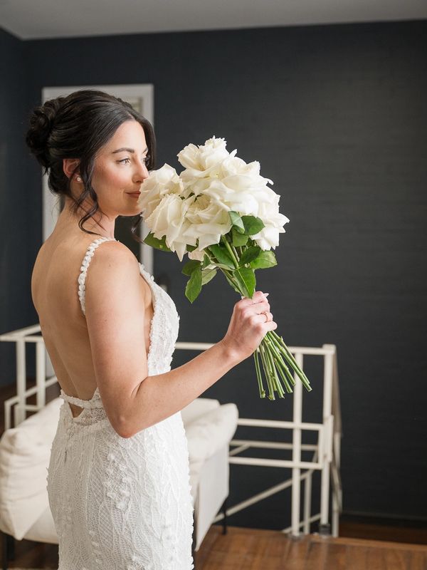 Bride in a white lace dress holding a bouquet of white roses.