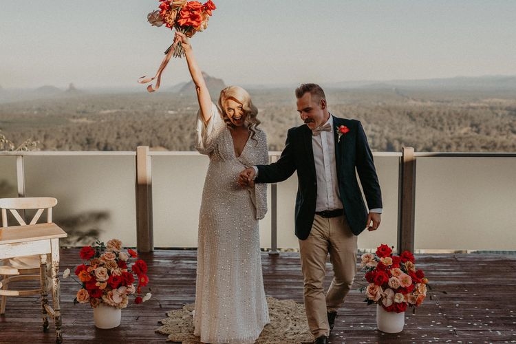 Bride and groom joyfully celebrating their wedding outdoors with floral decorations.