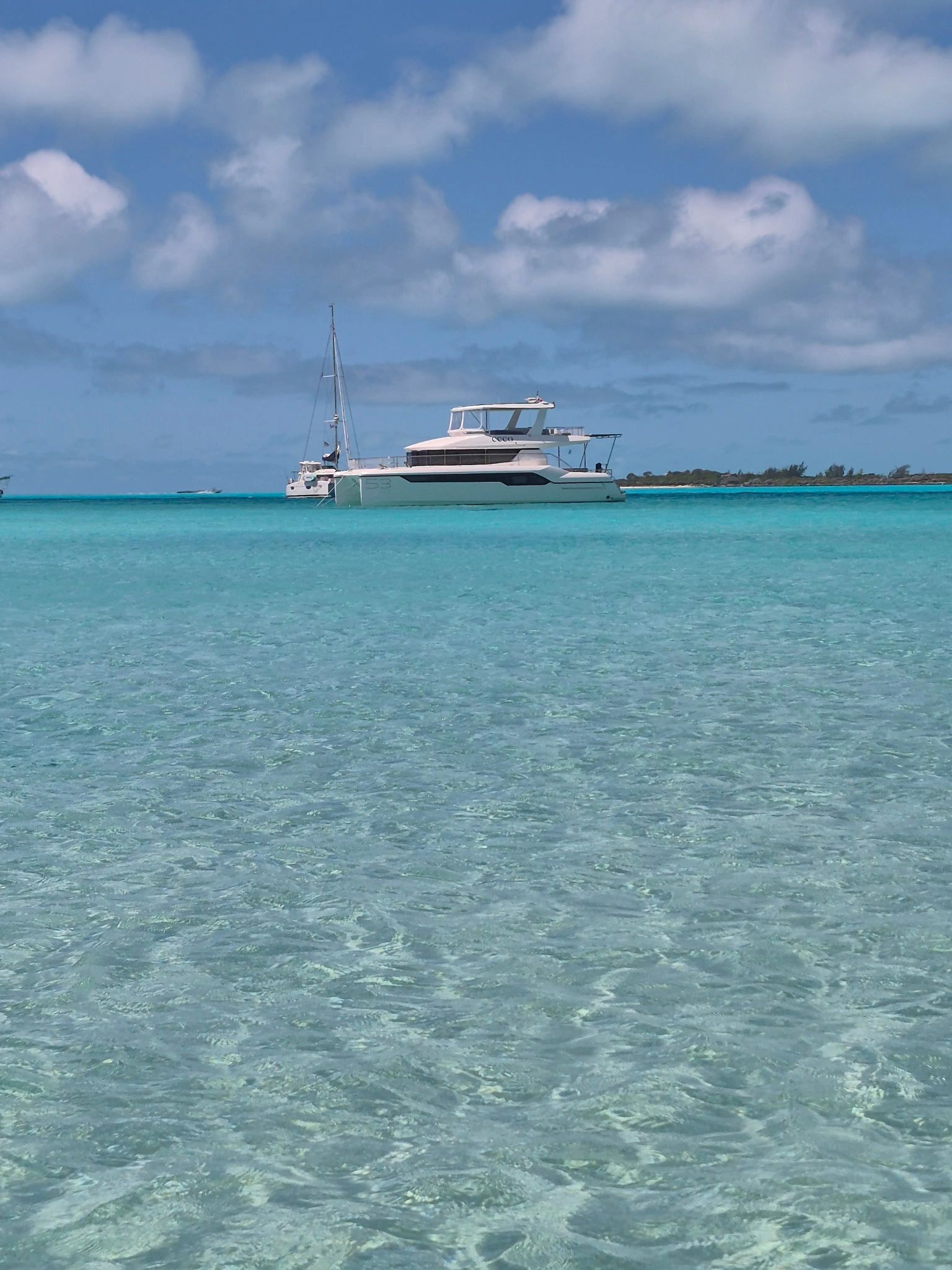 A white yacht anchored in clear turquoise waters under a partly cloudy sky.