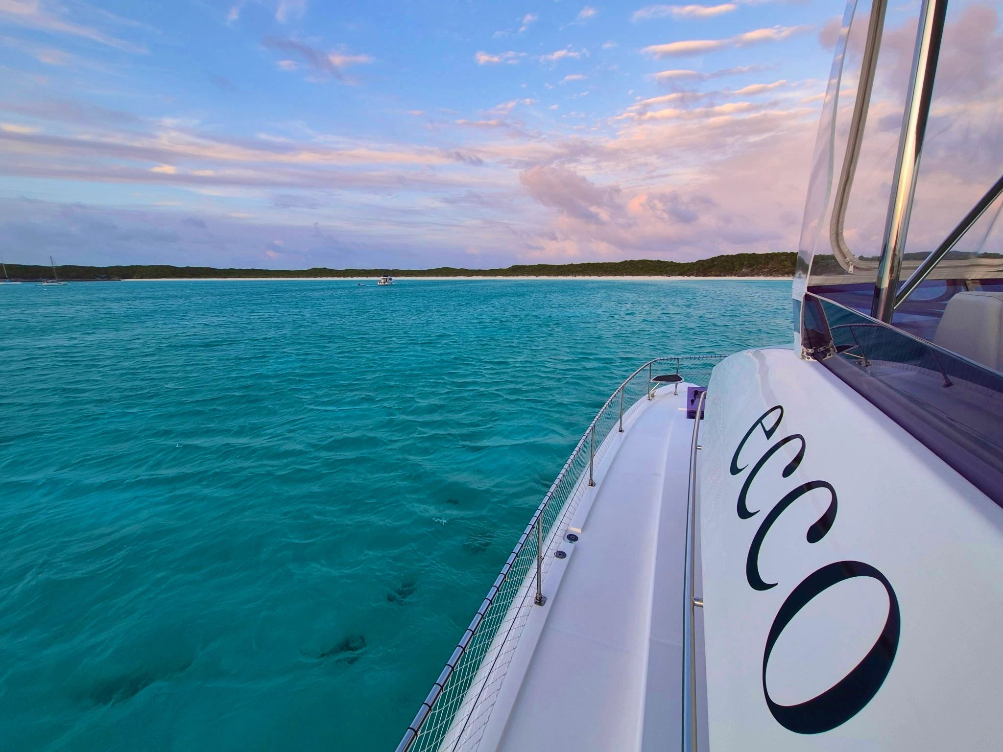 View from a boat on turquoise water with a scenic island and pastel sky.