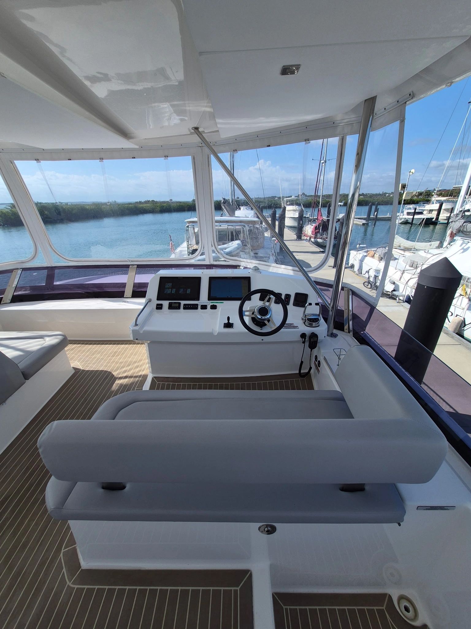 View of a boat's helm with a steering wheel and navigation screens overlooking a marina.
