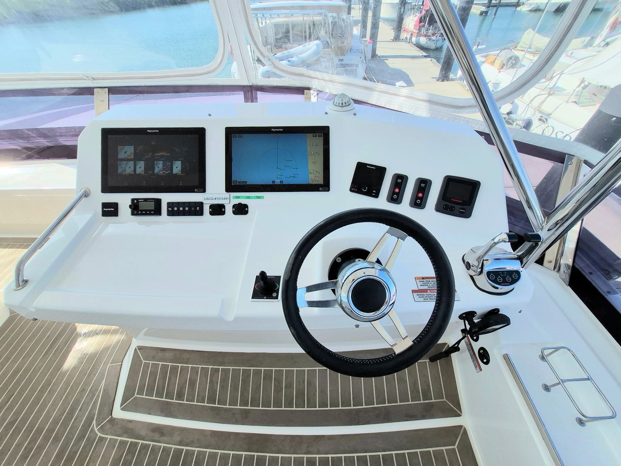 Boat helm with navigation screens and steering wheel at a marina.