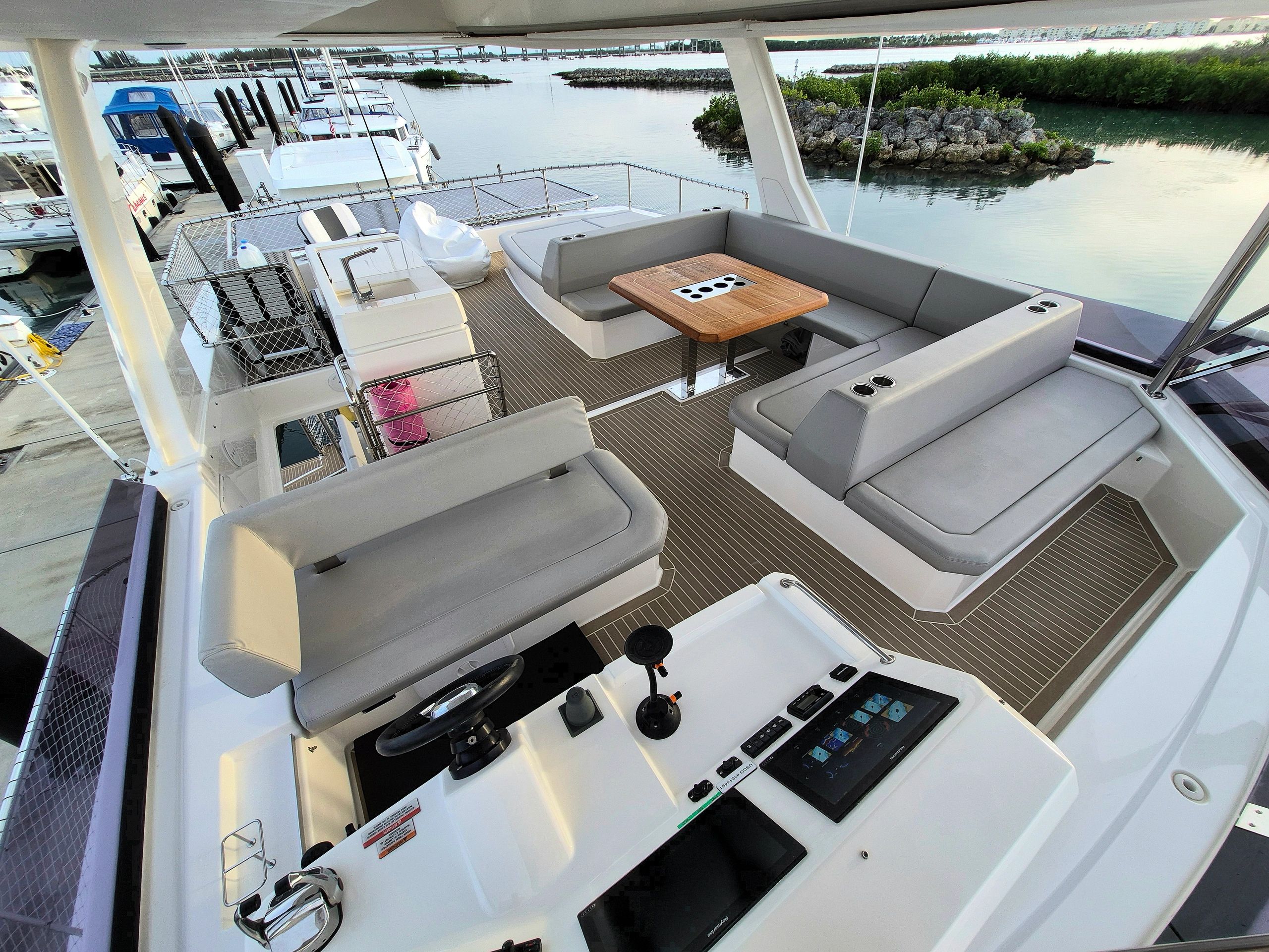 Modern yacht deck with seating, table, and helm station overlooking calm marina waters.