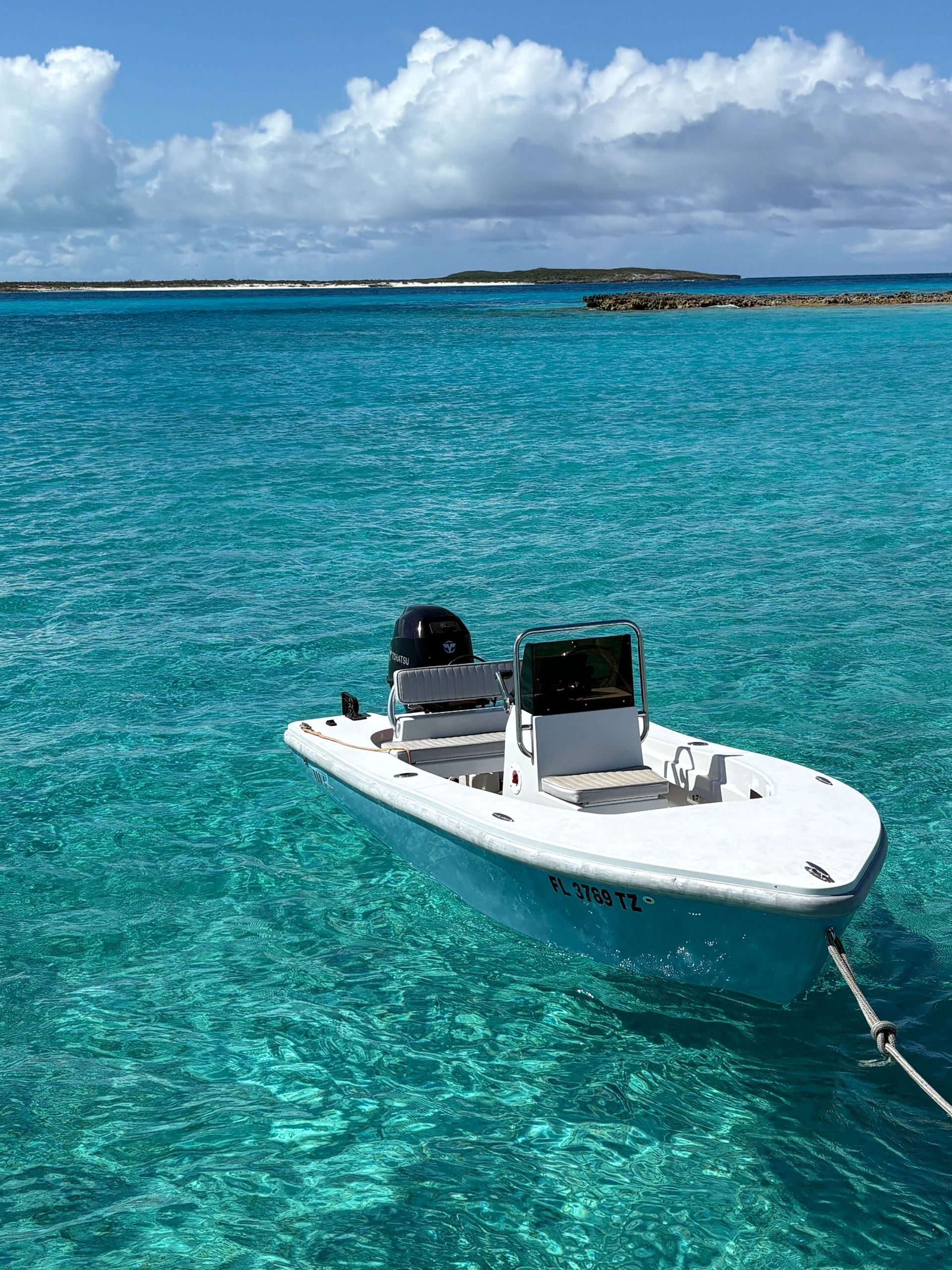 Small boat floating on clear turquoise ocean water near a rocky island.