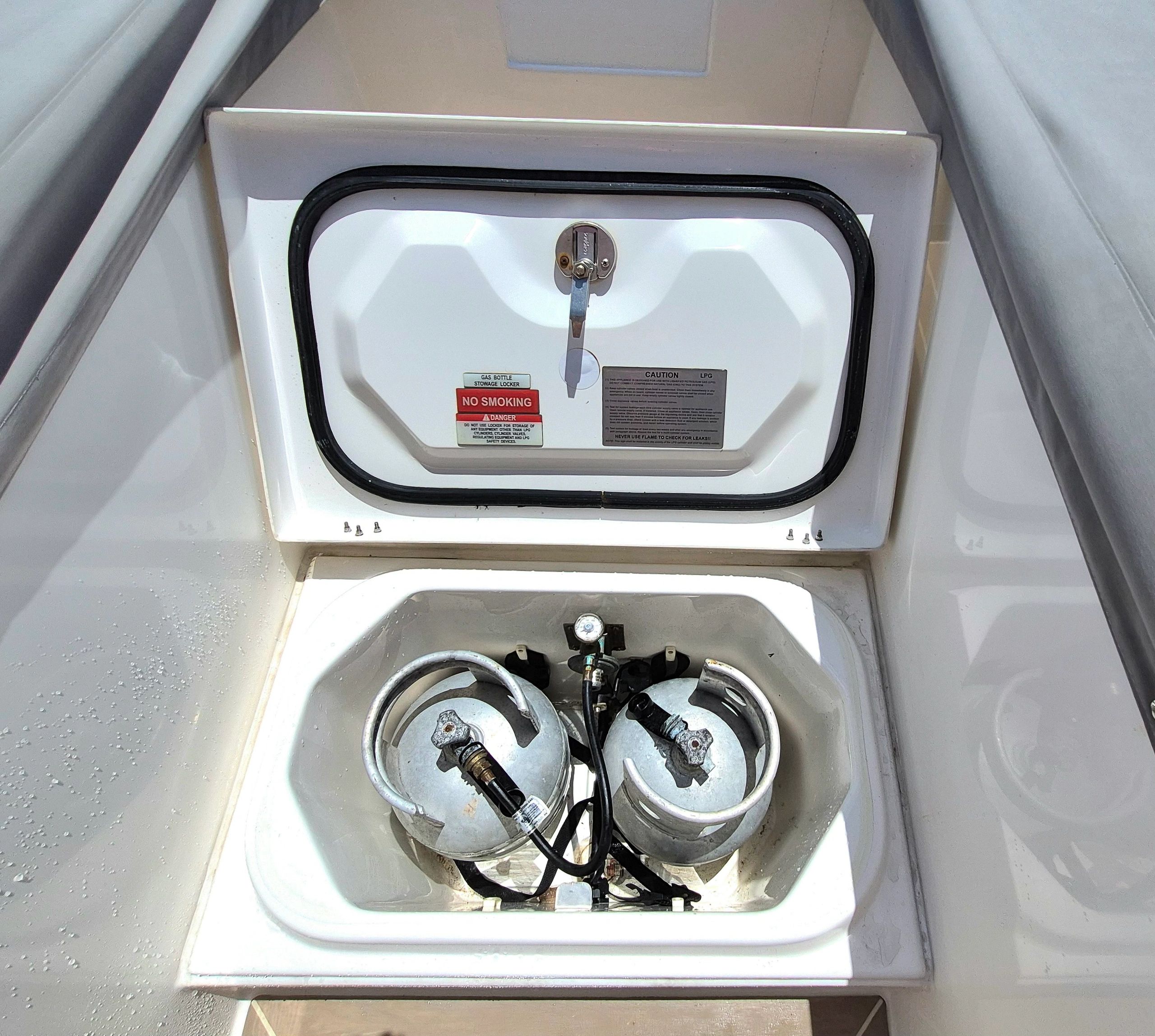 Boat storage locker containing two LPG gas cylinders with safety warnings.