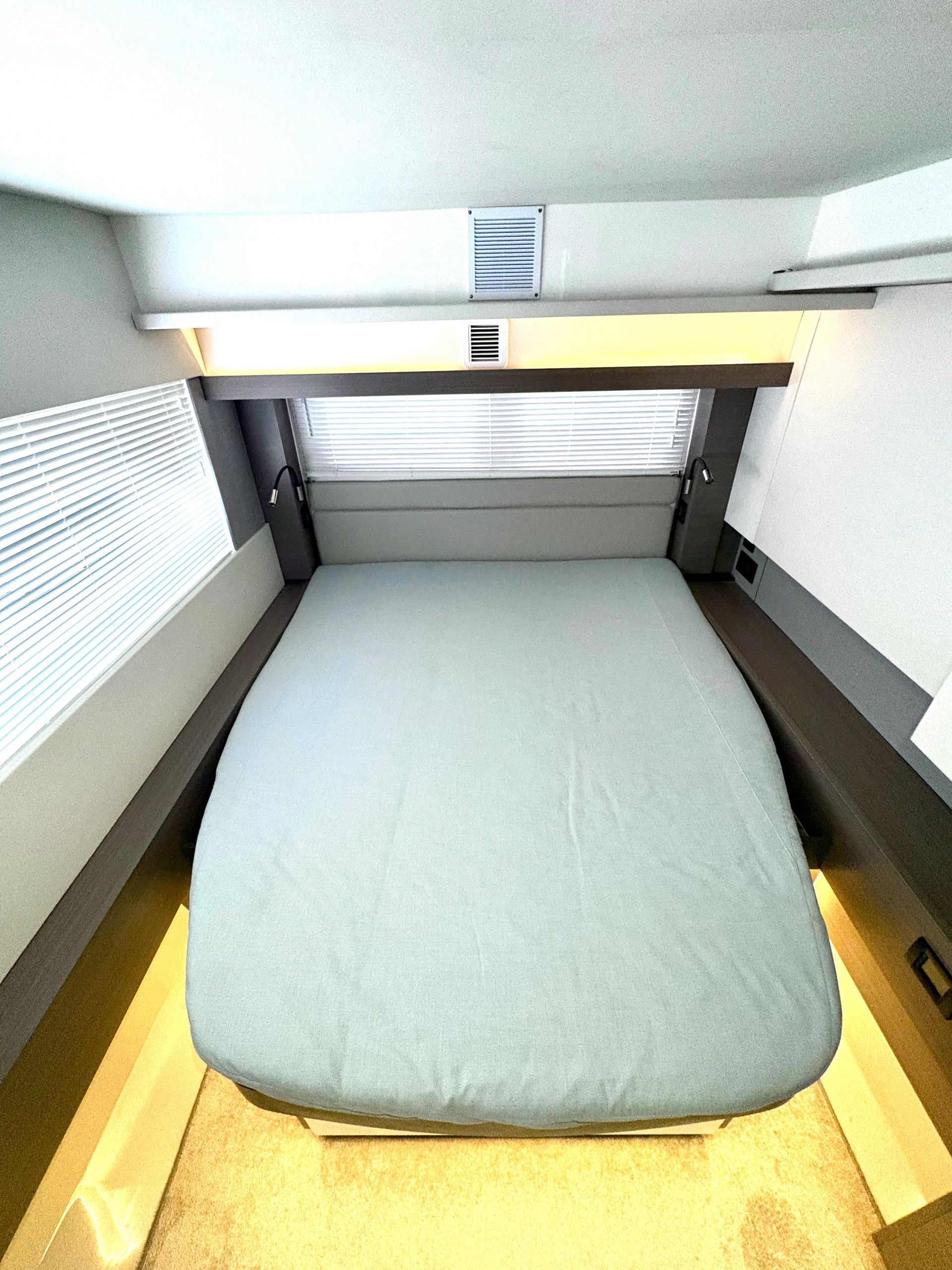 Compact, modern bedroom with a neatly made bed and bright window blinds.