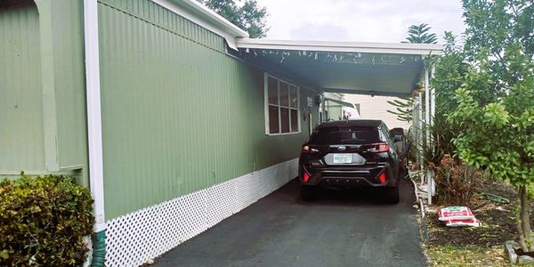 Black car parked under a green mobile home's carport.