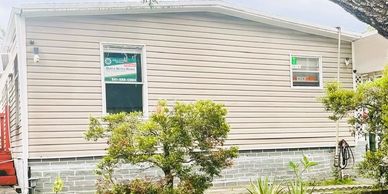 A single-story house with beige siding and greenery in front.