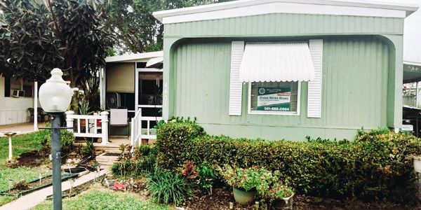 Green mobile home with a garden and a 'For Sale' sign.