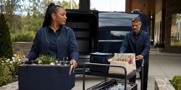 Two people unloading supplies from a vehicle outdoors.