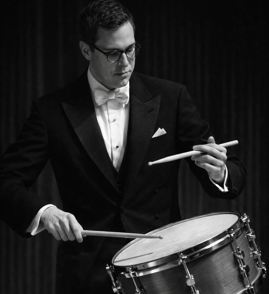 Man in tuxedo playing a snare drum with drumsticks.