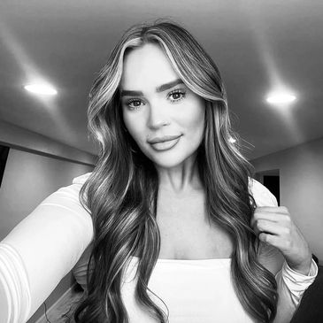 Young woman with long wavy hair taking a selfie indoors.