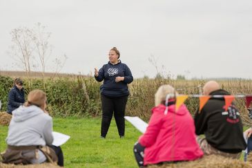 Outdoor speaker addressing a small seated audience on a cloudy day.