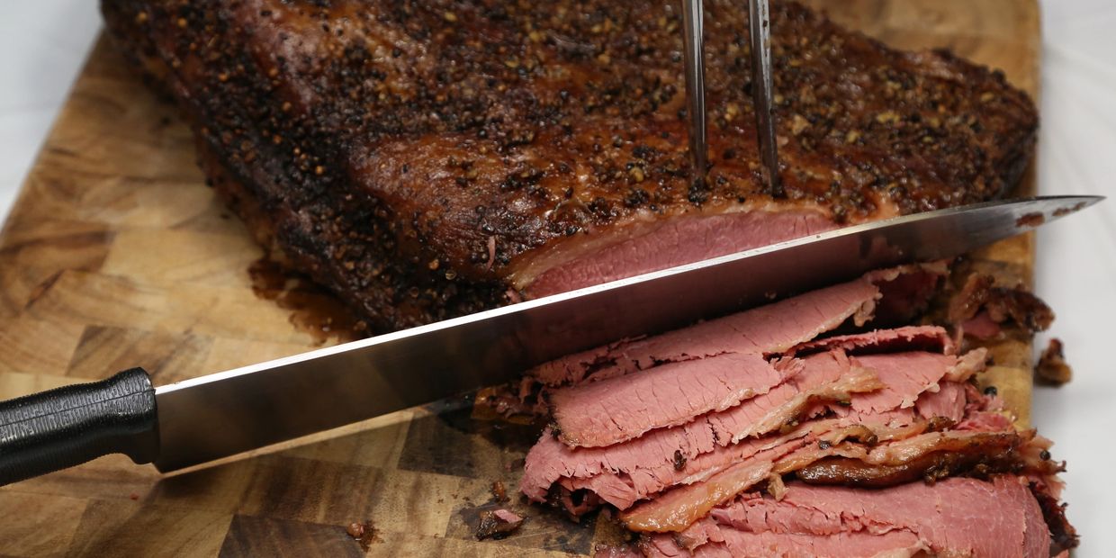 Slices of seasoned pastrami being cut on a wooden board.