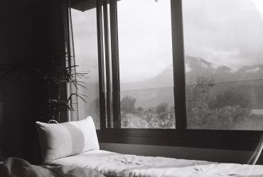 Sunlit bed near window with mountain view.