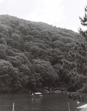 Boat on river near dense forested hill.