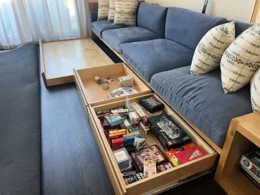 Pull-out drawer storage under a couch filled with various items.
