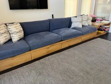 Long blue cushioned wooden sofa with white pillows.