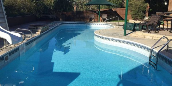 A clear blue swimming pool with a slide and seating area in a backyard.