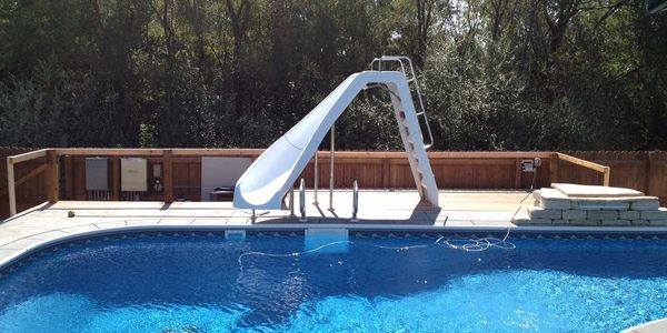Outdoor swimming pool with a white slide and wooden fence.