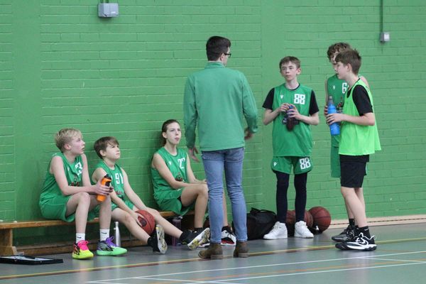 Wrexham Warriors basketball team listening to their basketball coach during a timeout on a basketball court.