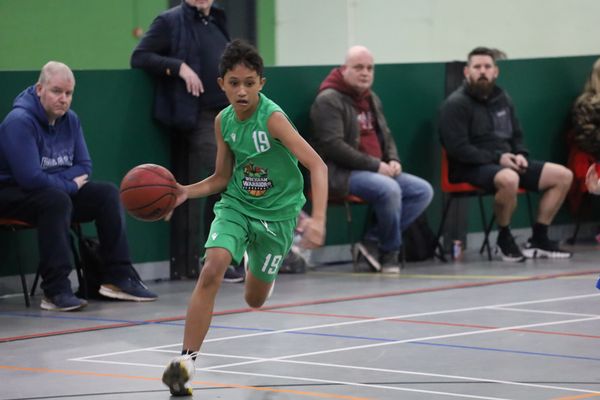 Young basketball player dribbling the ball during a game indoors.