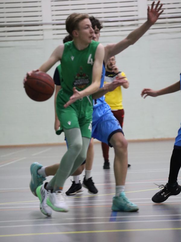 Young basketball player in green dribbling past defenders indoors.