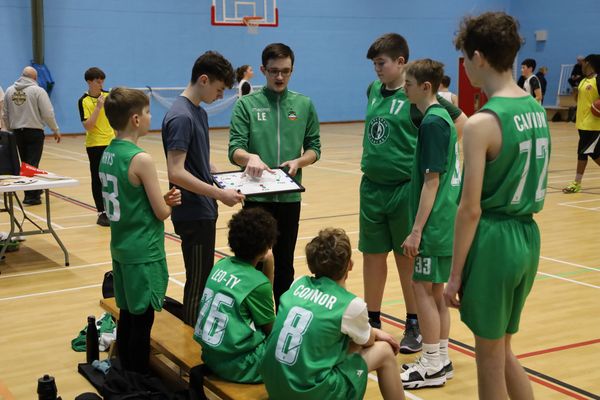 Youth basketball team receiving coaching during a timeout in a gym.