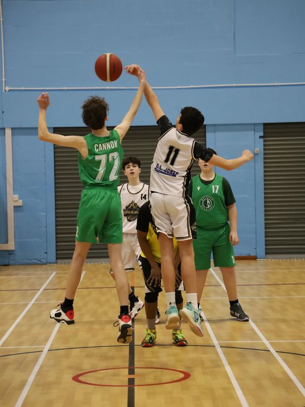 Two young basketball players jump to tip off the game on an indoor court.