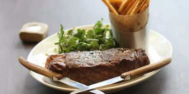Grilled steak served with fries and greens on a white plate.