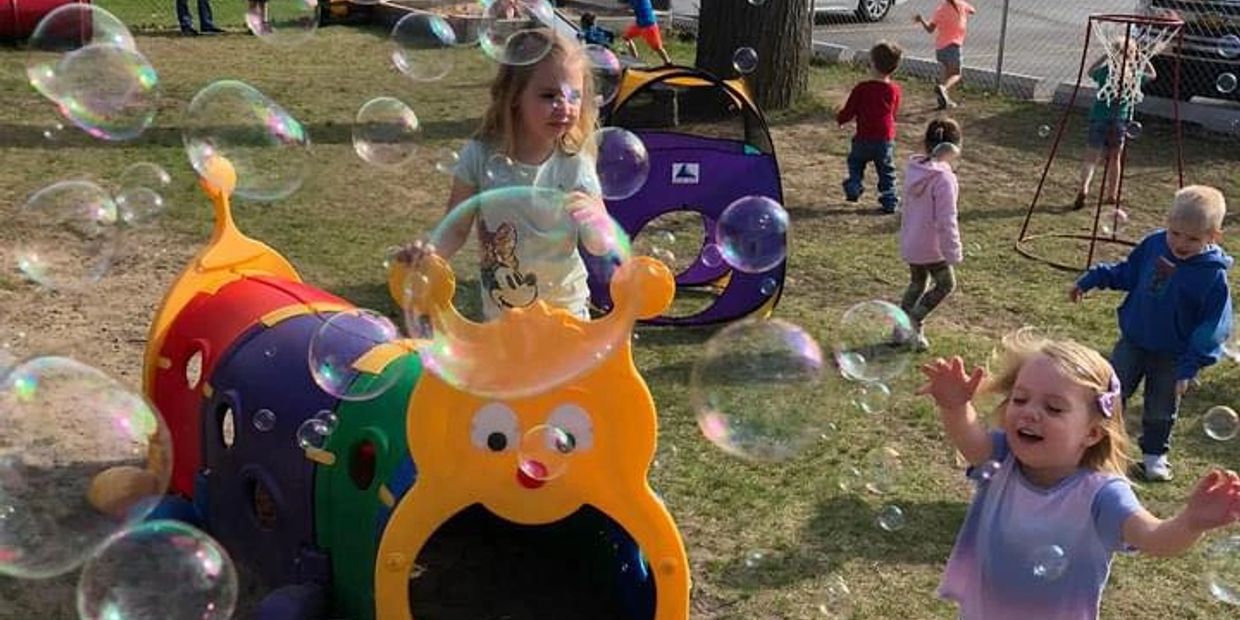 Children playing with bubbles and colorful playground toys outside.