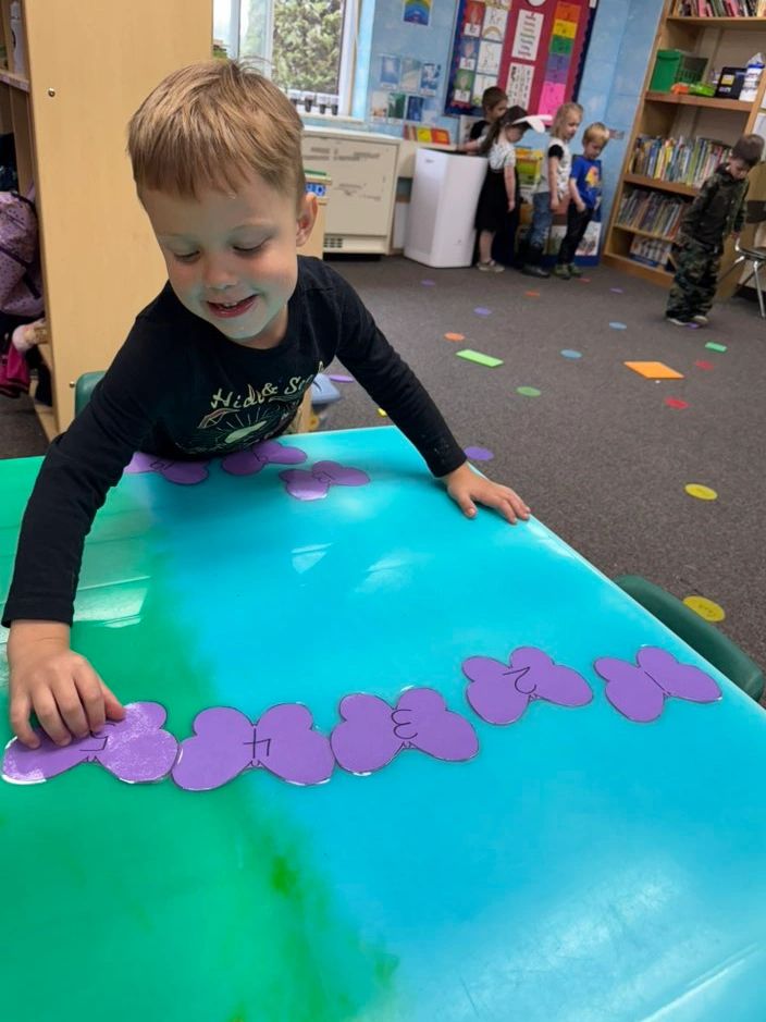 A boy arranges numbered purple butterfly cards on a blue-green table in a classroom.