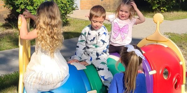Four children playing on colorful playground equipment outdoors.