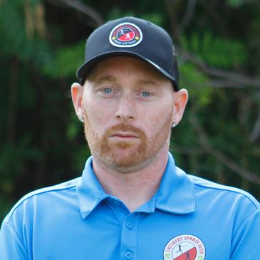 Man in blue polo and black cap with sports logo outdoors.