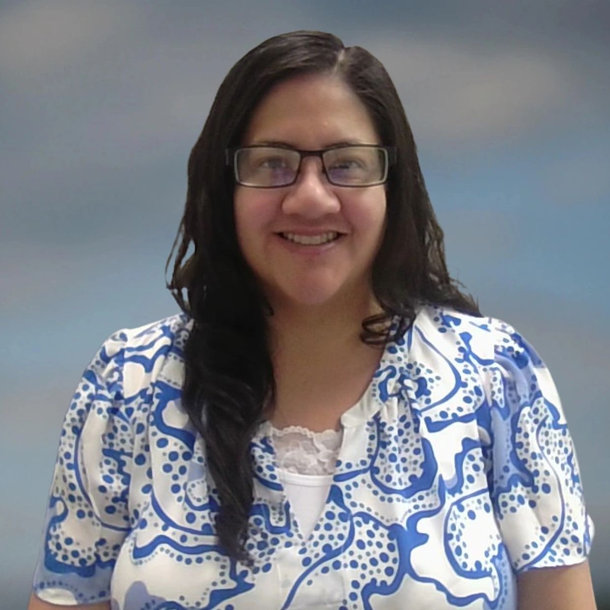 Woman smiling, wearing glasses and a blue-and-white patterned shirt.