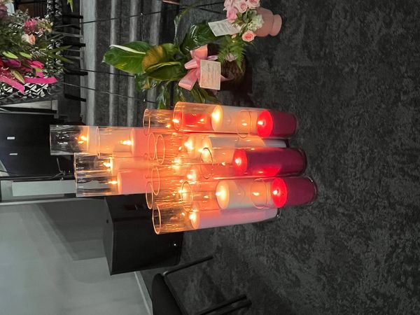 Lit candles in glass holders arranged on the floor near flowers.