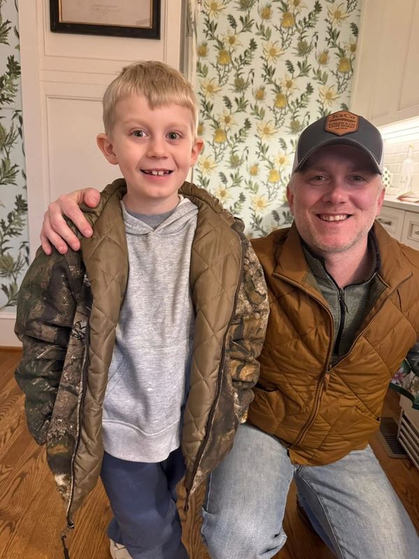 A smiling man and boy in warm jackets indoors.