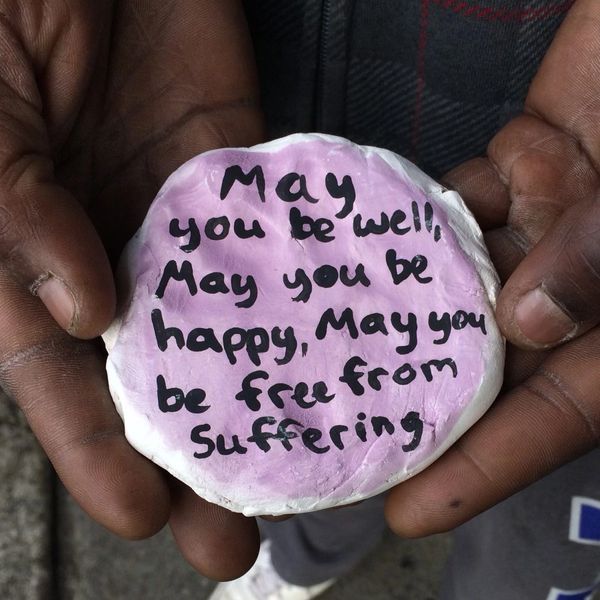 Hands holding a painted stone with a positive message of well-being and happiness.