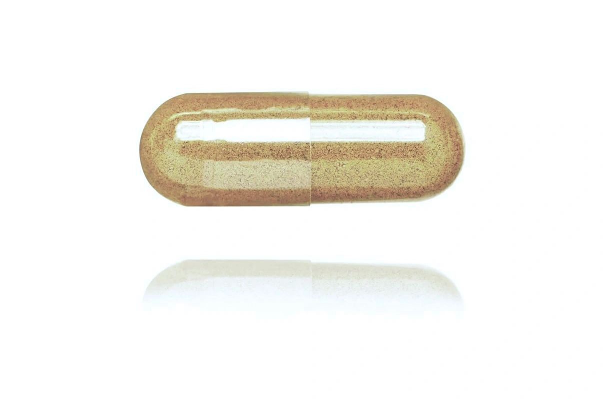 A single transparent capsule filled with brown powder on a white background.
