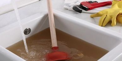 A clogged sink with dirty water and a plunger inside.