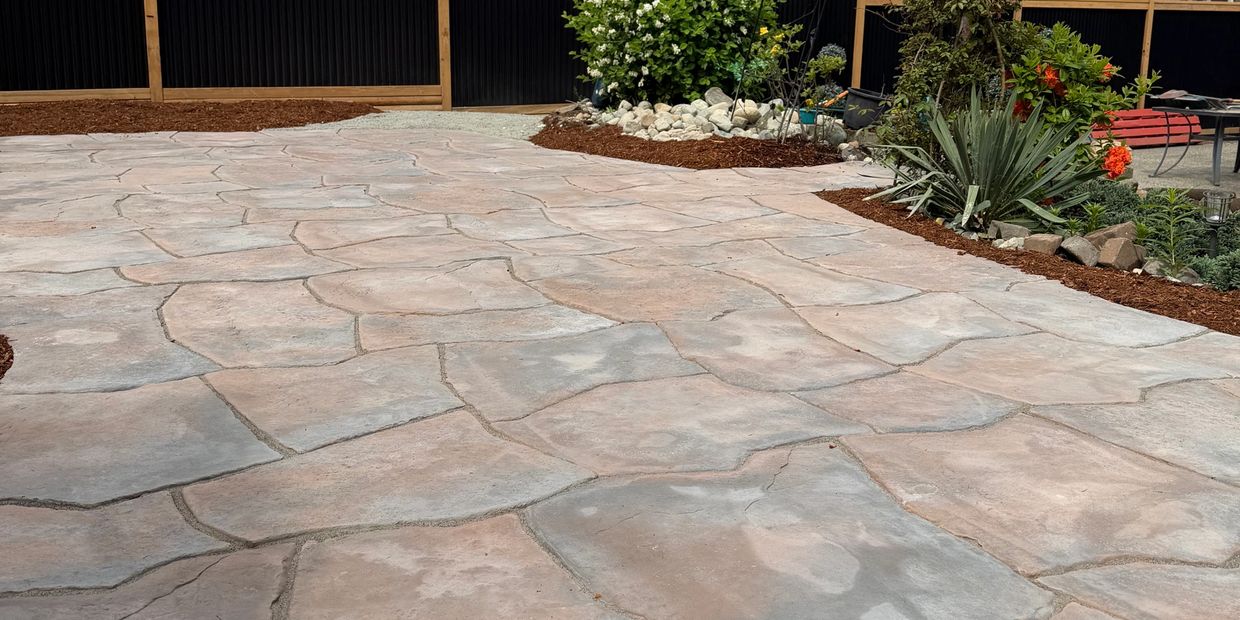 A stone-paved patio with surrounding garden and fence.